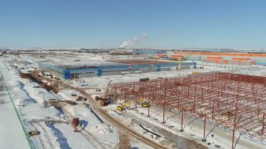 Kırmızı metal iskeletin yakınında vinç ve makineler var.