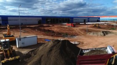 İnşaat alanındaki bitmemiş deponun yakınında makineler çalışıyor.