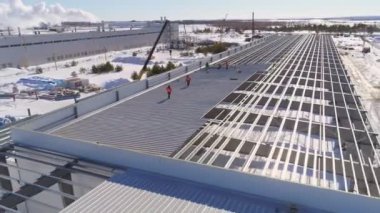 İnşaatçılar kışın atölyenin bitmemiş çatısında yürürler.