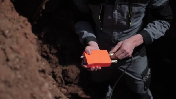 Worker connects cable to seismographical sensor in trench — Stock Video