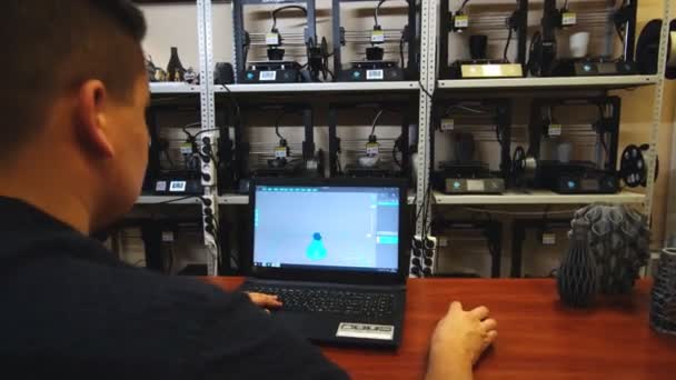 Designer zeichnet Modell auf Laptop in der Nähe von Regalen mit 3D-Druckern — Stockvideo