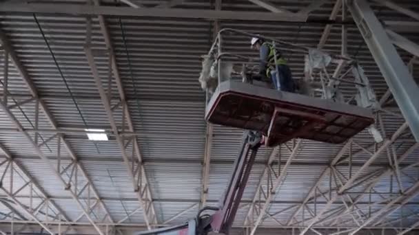 Werknemer staat in hefwieg onder het plafond van de werkplaats — Stockvideo