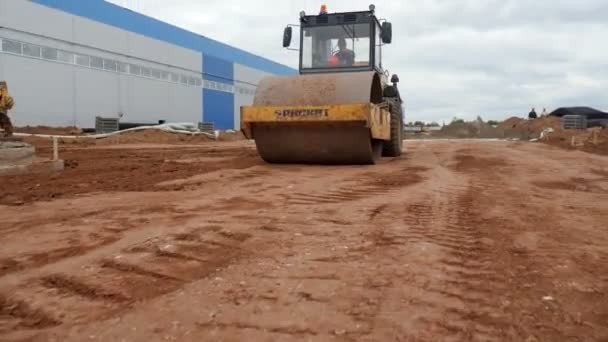 Silniční válec projíždí kolem nedokončeného skladu podél místa — Stock video