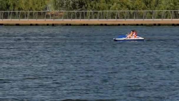 Junge Frauen fahren an windigem Tag Tretboot flussaufwärts — Stockvideo