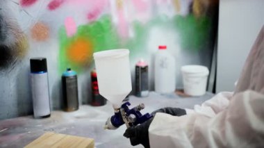 Masadaki sprey tabanca kabına beyaz boya dökülüyor.