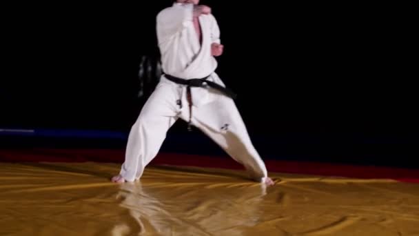 Joven en kimono blanco salta haciendo ejercicio de karate en el gimnasio — Vídeos de Stock