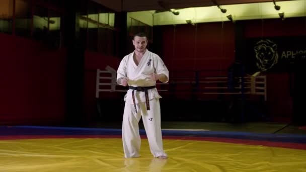 Deportista en kimono muestra patadas en las piernas saltando en un amplio gimnasio — Vídeos de Stock