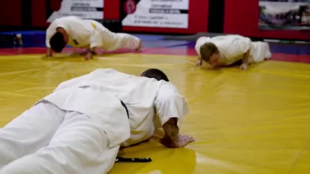 Deportistas en kimonos realizan flexiones en la esterilla en un amplio gimnasio — Vídeos de Stock