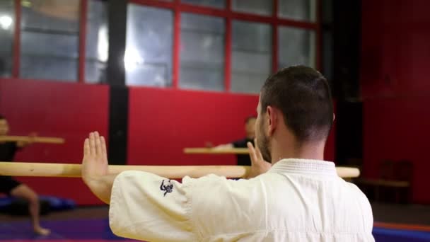 Man in kimono en studenten doen oefeningen met stokken in de sportschool — Stockvideo