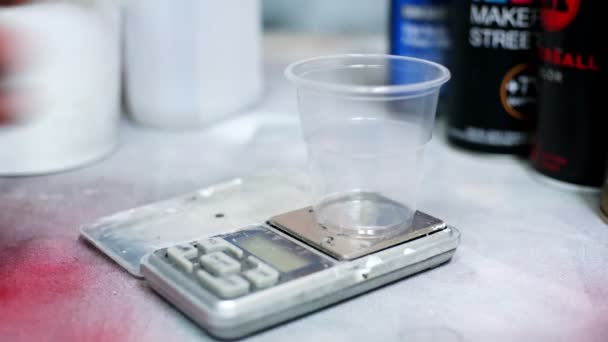 Чоловік кладе порожню чашку на цифровий масштаб і наливає білу фарбу — стокове відео
