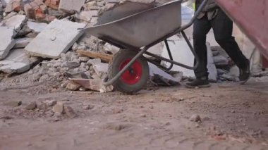 İşçi, el arabasının içinde ağır beton parçaları itmeye çalışıyor. İşçi beton bloğu taşırken demir el arabası gıcırdıyor