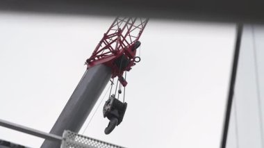 Kule vinci bulutlu, kasvetli gökyüzüne doğru yükseliyor. Ağır sallanan kanca yavaşça hareket ederek endüstriyel dinamik atmosfer yaratır