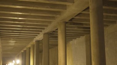 Kaburgalı tavanın altından beton sütunlar yükseliyor soluk sarı parıltıyla aydınlatılıyor. Kıt tasarım gizemli bir yeraltı atmosferi yaratır