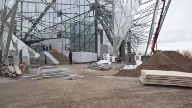 Üçgen cam tesisleri olan bina bulutlu gökyüzünün altında yükseliyor. Devam eden kentsel gelişime ilişkin inşaat işaretlerinin etrafındaki izler