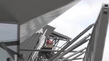 Metalik kirişlerden oluşan yoğun ağlar vasıflı işçilerin dış görünüşü. İnsan çabası sert geometriyle hassas zanaatkarlığı zıtlaştırır.