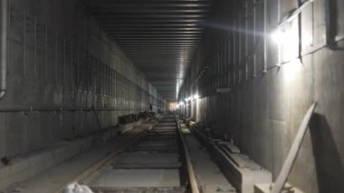 Demiryolları loş lambalarla aydınlatılan metro tünelinin derinliklerine uzanıyor. Dağılmış nesneler inşaat alanının ham gerçekliğini vurguluyor. Metro inşaatı