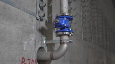 Disk kapakçığı ile donatılmış metal boru beton duvarla kaplıdır. Yakındaki elektrik tesisatı için kancalar endüstriyel tasarımın düzenli ritmini oluşturuyor