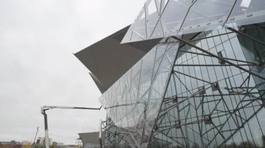 Cam cephe, bulutlu dramatik gökyüzünü yansıtır ve dengesiz duygusal atmosfer yaratır. Dekoratif yapının ağ deseni sanatsal geometri ekler