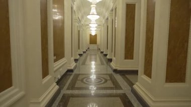 Koridor, parlak avizelerin altındaki büyük tahta sütunlarla kaplı. Kristal ışık cihazları cilalanmış zemin uyumunu vurgular