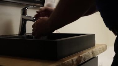 Banyodaki lavaboda ellerini yıkayan adam. Krom çelik banyo musluğundan su akar. Kapat, yavaşça yakınlaştır. Güçlü su akışı.