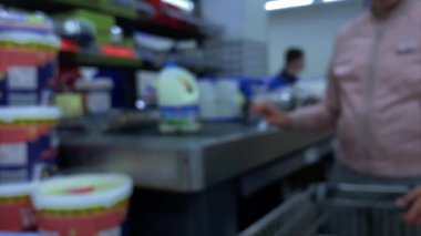 Mavi. Yaklaş. Alıcı, marketteki kasanın yanındaki konveyör bandındaki sepetteki yiyecekleri yerleştiriyor.