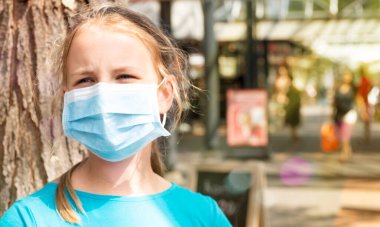 Sıcak bir yaz gününde üzgün bir kız karantina sırasında şehir caddesinde tıbbi maske takar. Covid-19 salgını sırasında şehir 