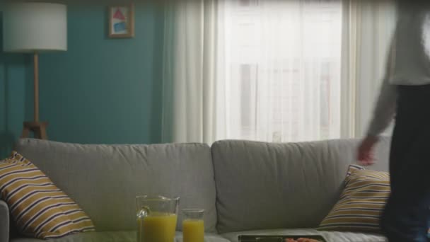 Chica joven con el pelo rubio se sienta en el sofá beige y toma palos de sushi para comer — Vídeos de Stock