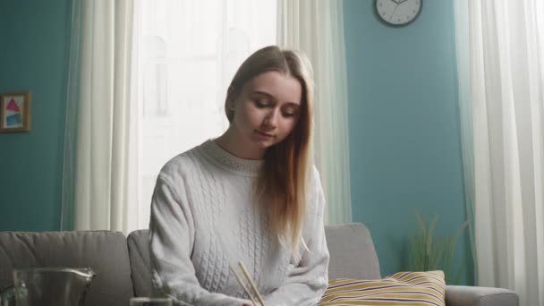 Chica joven con el pelo rubio y suéter blanco toma palillos de sushi y come — Vídeo de stock