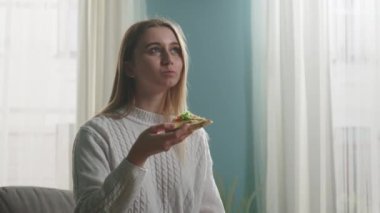 Bej bir kanepede elinde pizza tutan genç bir kız.
