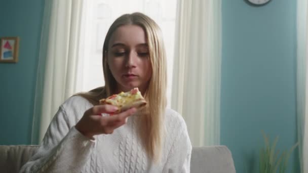 Chica en un suéter blanco se come una rebanada de pizza italiana — Vídeo de stock