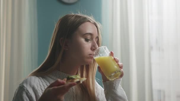 Jong meisje in witte trui eet pizza en drinkt sinaasappelsap — Stockvideo