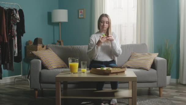 Jong meisje in een witte trui bijt een stuk pizza — Stockvideo