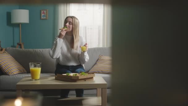 A fehér kabátos lány pizzát eszik és narancslevet iszik. — Stock videók