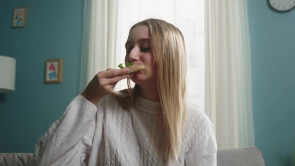 Chica en un suéter blanco se come una rebanada de pizza italiana — Vídeos de Stock