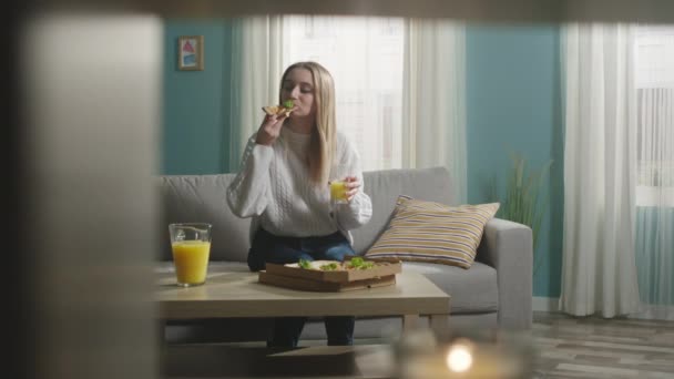 A fehér kabátos lány narancslevet iszik és pizzát eszik. — Stock videók