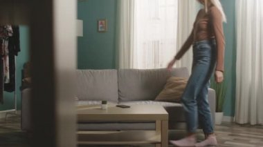 Genç bir kız odaya girer, kanepeye oturur ve telefonu alır.