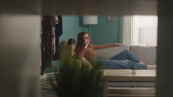 Unga dam ligger på soffan och ivrigt pratar i telefon — Stockvideo