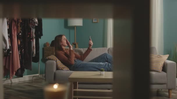 Jeune fille couchée sur le canapé et téléphone parlant via lien vidéo — Video