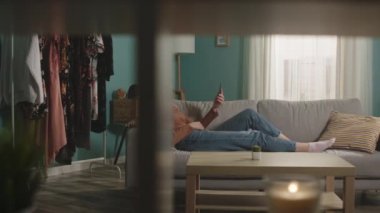 Genç kız kanepede uzanıyor ve video bağlantısıyla telefonla konuşuyor.