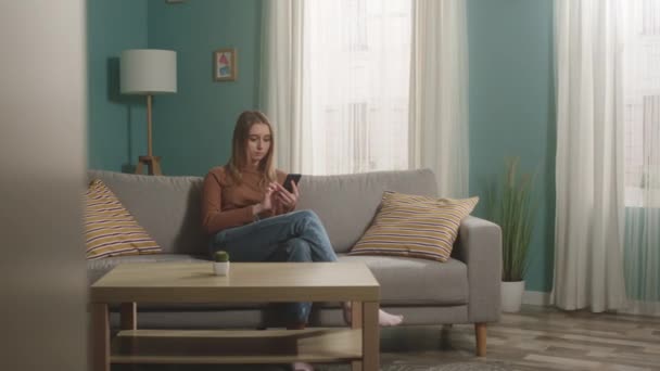 Menina sentada no sofá e falando telefone via link de vídeo — Vídeo de Stock