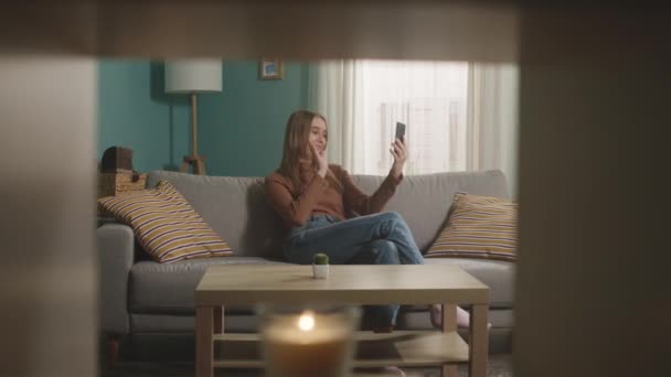 Junges Mädchen sitzt auf der Couch und telefoniert per Videolink — Stockvideo