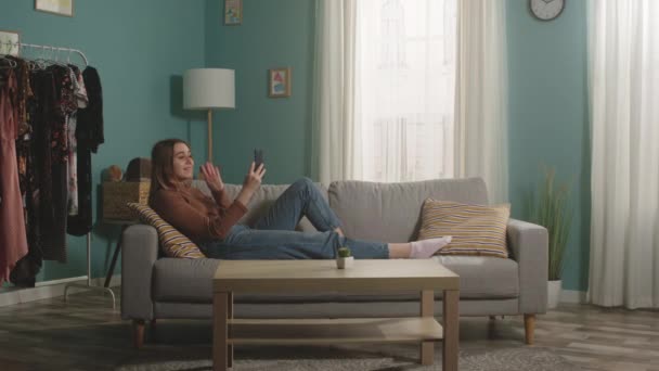 Jeune fille couchée sur le canapé et téléphone parlant via lien vidéo — Video