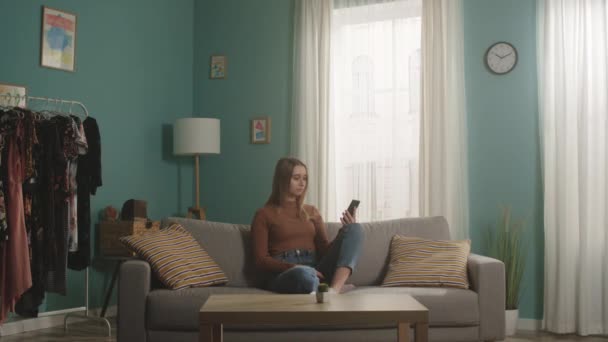 Junges Mädchen sitzt auf einem Sofa und telefoniert per Videolink — Stockvideo