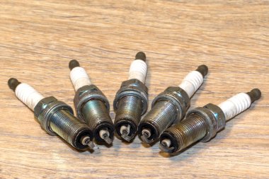 Four old used and dirty spark plugs from a car. On wooden background clipart