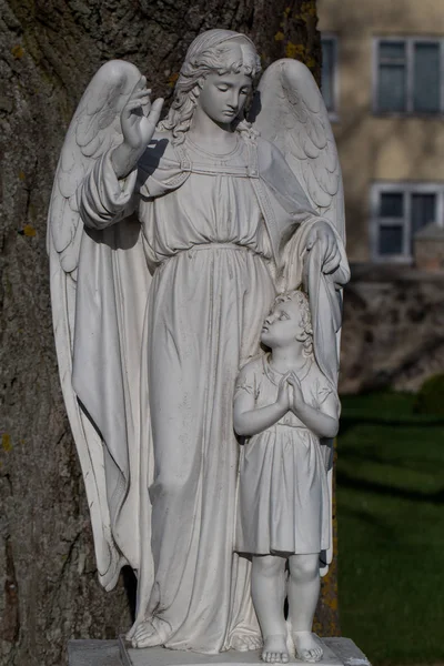 Beautiful ancient female angel sculpture with a child in front of a old tree in the garden