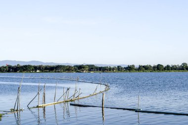Kafeslerdeki tatlı su balıkları, göl manzarası, suya yansıyan bulutlar.