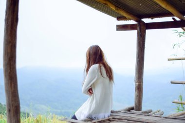 Genç yalnız kadın kulübede oturuyor ve doğaya bakıyor, tatilde dinleniyor.