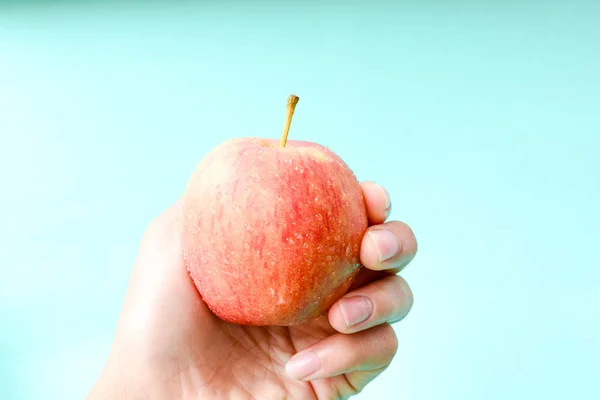 hand holding apple on blue background with copy space, healthy concept