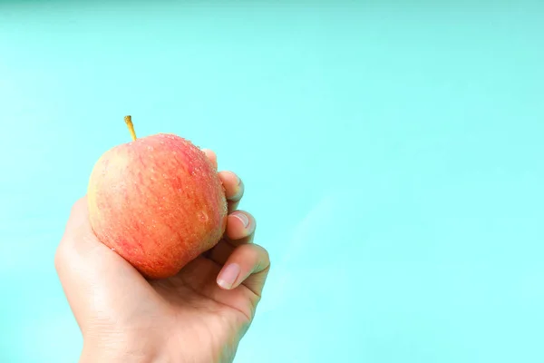 hand holding apple on blue background with copy space, healthy concept