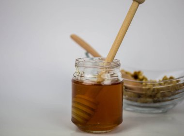 Beyaz arka planda bal ve ceviz. Bal için tahta sopa. Doğal olarak en sağlıklısıdır.